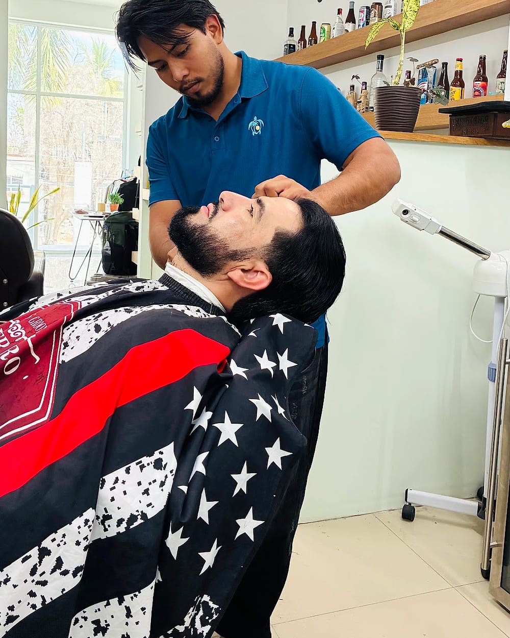 Barbero arreglando la barba de un cliente con capa de bandera